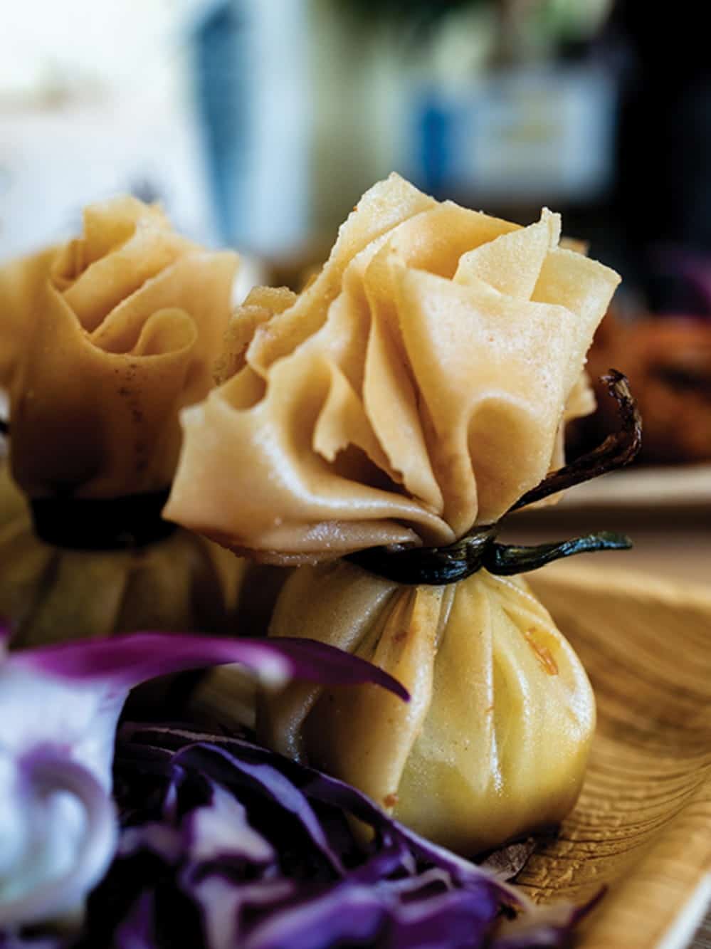 Close-up of two tied dumplings with pleated tops on a wooden plate, garnished with shredded purple cabbage—a delicious example of Seattle fusion Thai at Bloom Thai.