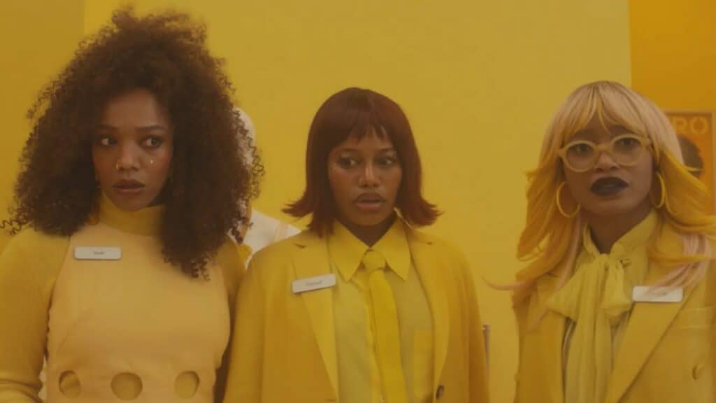 Three women in yellow outfits with name tags stand against a bright yellow background, all looking ahead with neutral or slightly surprised expressions—reminiscent of characters from must-see films at the Seattle International Film Festival.
