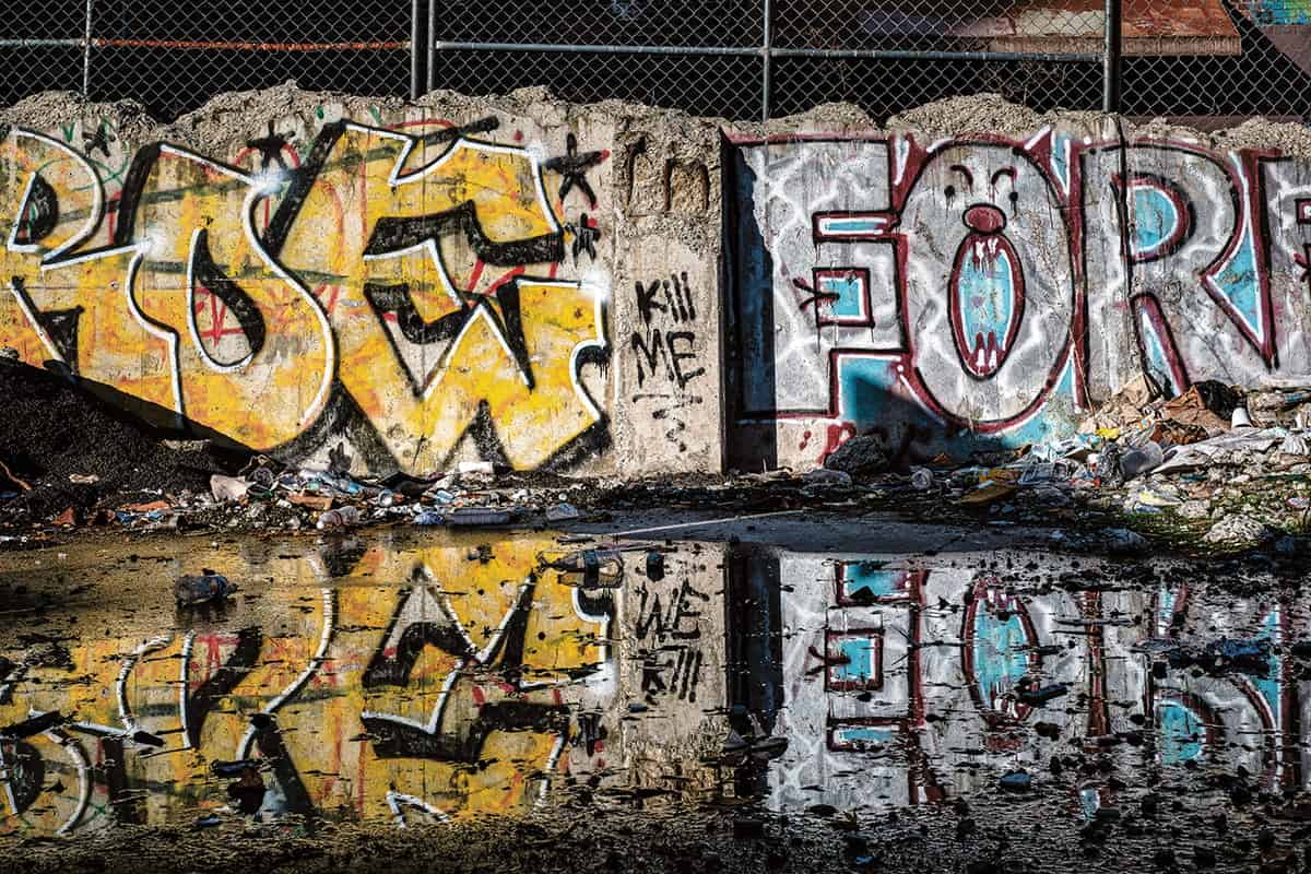 Graffiti covers a concrete wall behind a puddle of water in Pioneer Square, its reflection capturing the vibrant Seattle graffiti and scattered debris—an authentic scene of urban landscape photography.