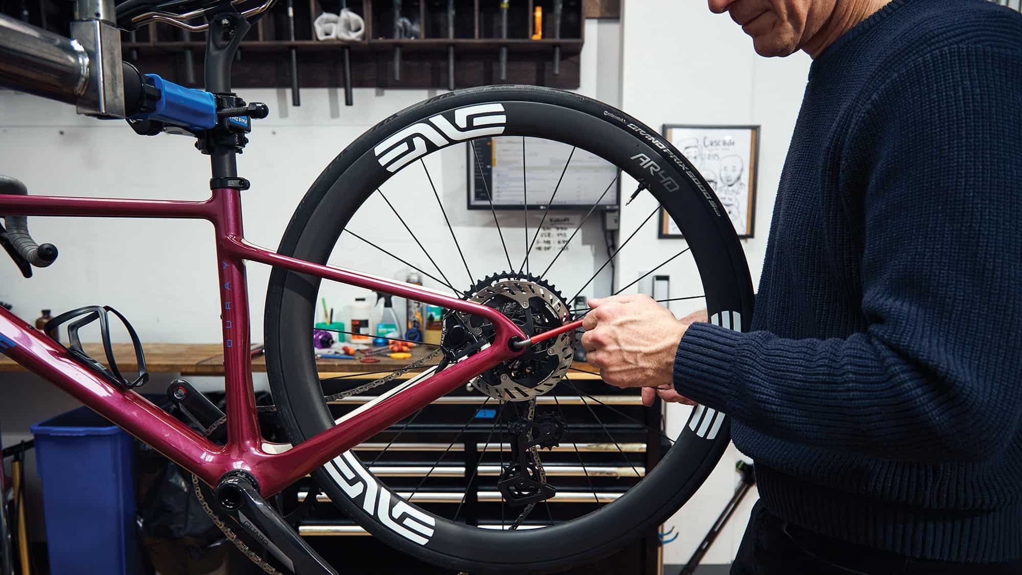 Person adjusting the rear derailleur on a red bicycle mounted on a repair stand in a workshop at ID Match Bike Lab, known for precision bike fit Seattle and custom bicycles Pacific Northwest.
