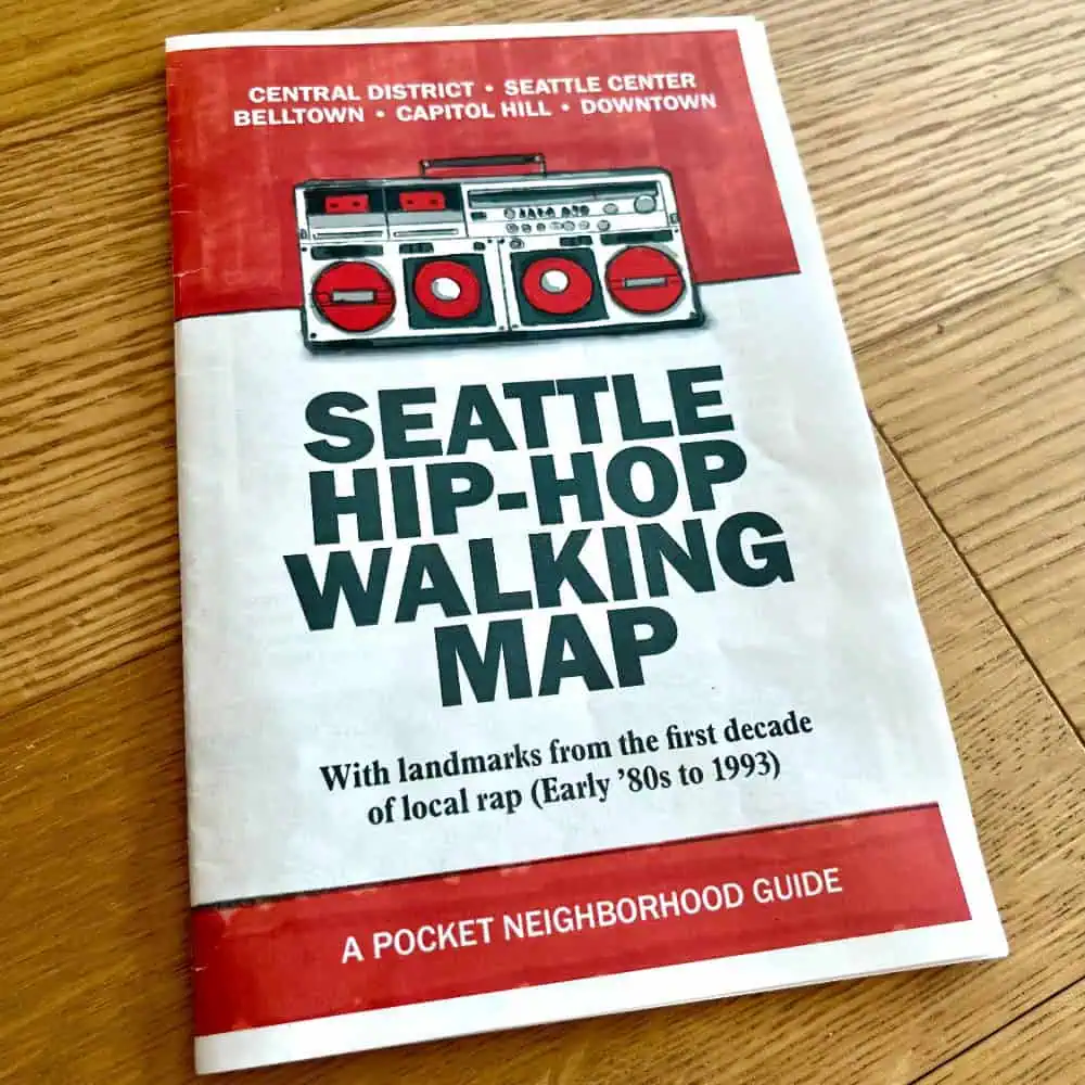 A booklet titled "Seattle Hip-Hop Walking Map" featuring a graphic of a boombox and text about local rap landmarks from the early '80s to 1993.