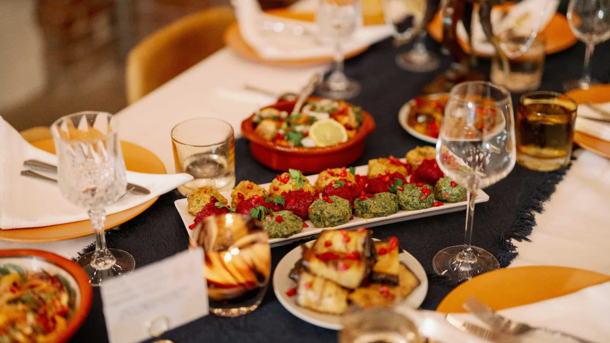A dinner table set with plates, glasses, and various colorful appetizers, including vegetables and garnished finger foods, arranged on serving dishes.