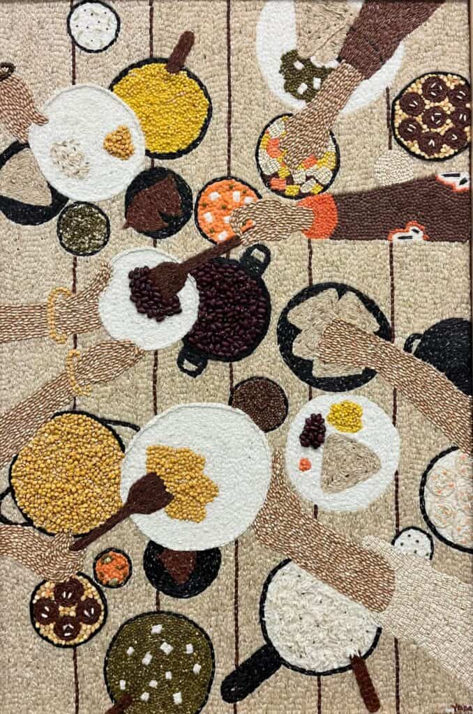 A top-down view of several hands reaching for plates and bowls filled with various foods on a patterned table.