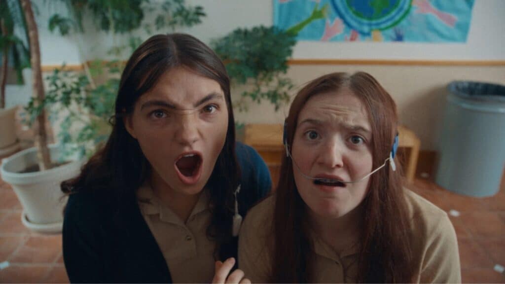 Two young women in school uniforms sit indoors; one looks angry with her mouth open, the other appears distressed and wears nasal cannulas—an intense scene worthy of movie recommendations at any film festival.