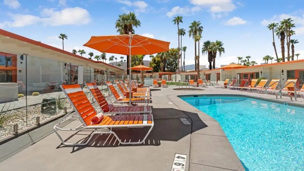A bright blue swimming pool is surrounded by lounge chairs and palm trees at a resort.