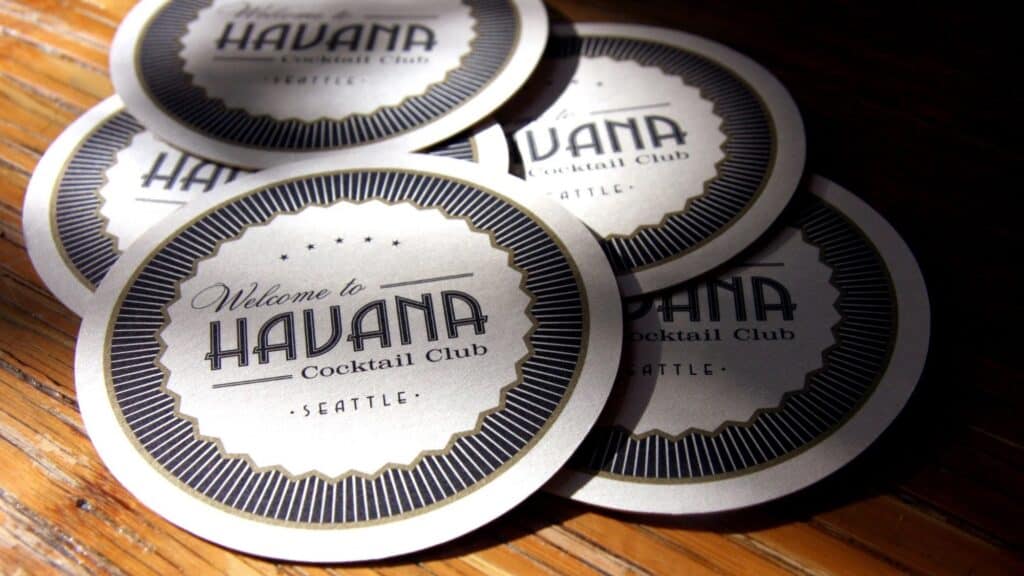 Round coasters on a wooden surface display "Welcome to Havana Cocktail Club Seattle" in bold text with a decorative border.
