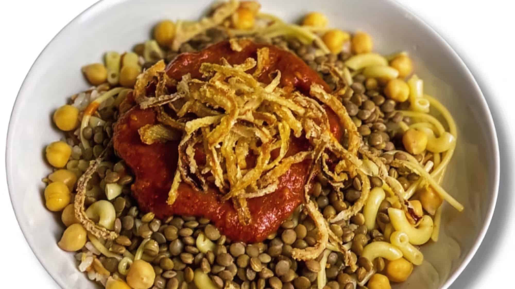 A bowl of koshari, Egypt’s national dish, with macaroni, rice, lentils, chickpeas, tomato sauce, and crispy fried onions on top.