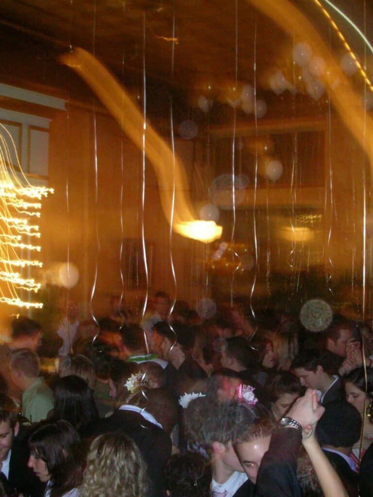 A crowded indoor party with people dancing; streaks of light and blurred motion indicate movement and dim lighting.