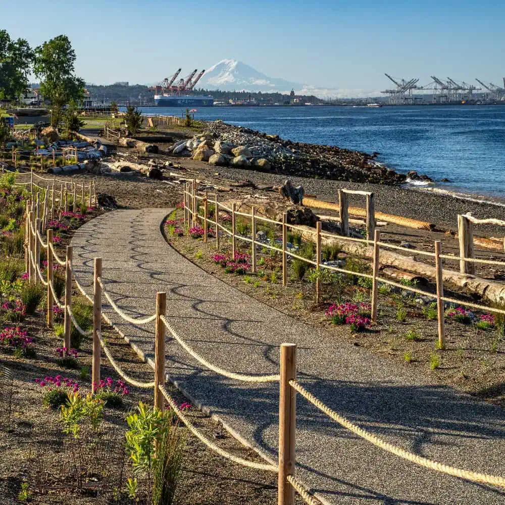A gravel path bordered by rope fencing curves along a waterfront with industrial cranes and a snow-capped mountain in the distance—perfect inspiration for your next Father’s Day Gift or to include in your ultimate Gift Guide.
