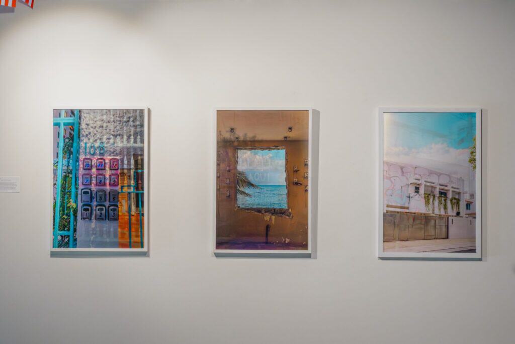 Three framed photographs are displayed on a white gallery wall, each depicting different urban and architectural scenes.