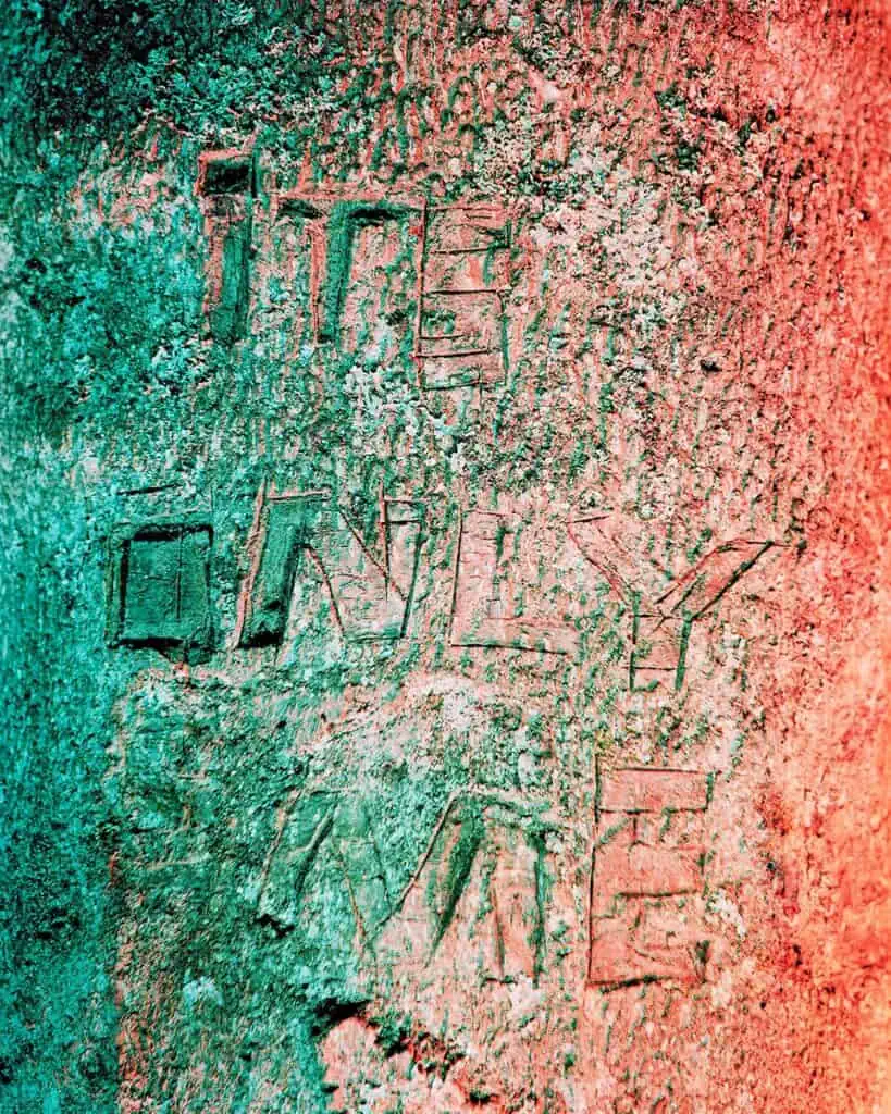 Rough stone surface with the words "IT'S ONLY ME" carved into it, illuminated by teal and red lighting.
