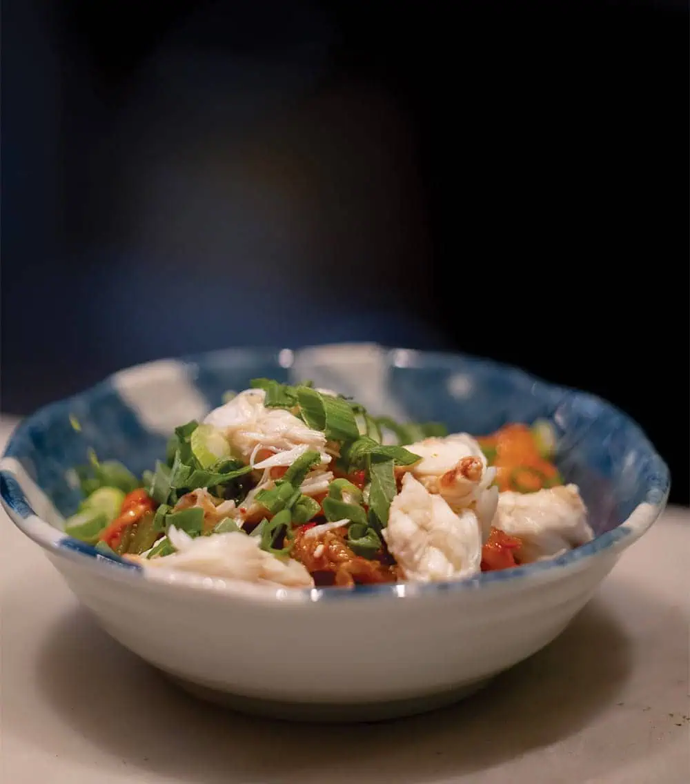 A bowl filled with cooked white fish, chopped green onions, and red peppers, served in a blue and white ceramic bowl on a light surface—a delightful dish reminiscent of the fresh flavors found at popular Capitol Hill dining spots.