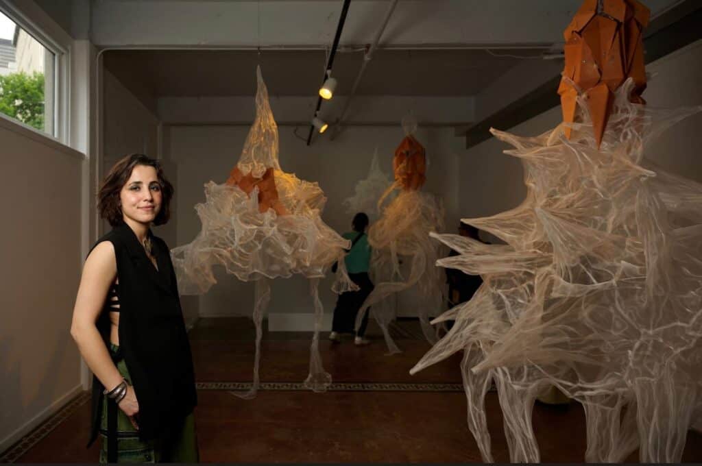A woman stands in an art gallery with translucent, spiky sculptural installations hanging from the ceiling.