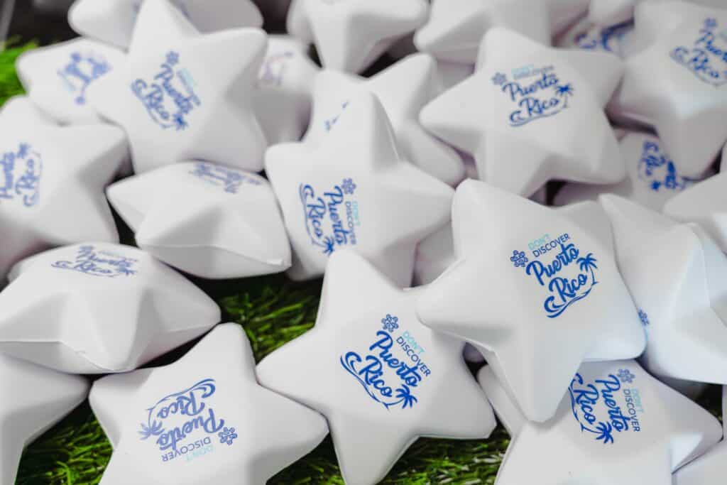 A pile of white star-shaped objects with "Discover Puerto Rico" printed in blue on each, resting on green artificial grass.