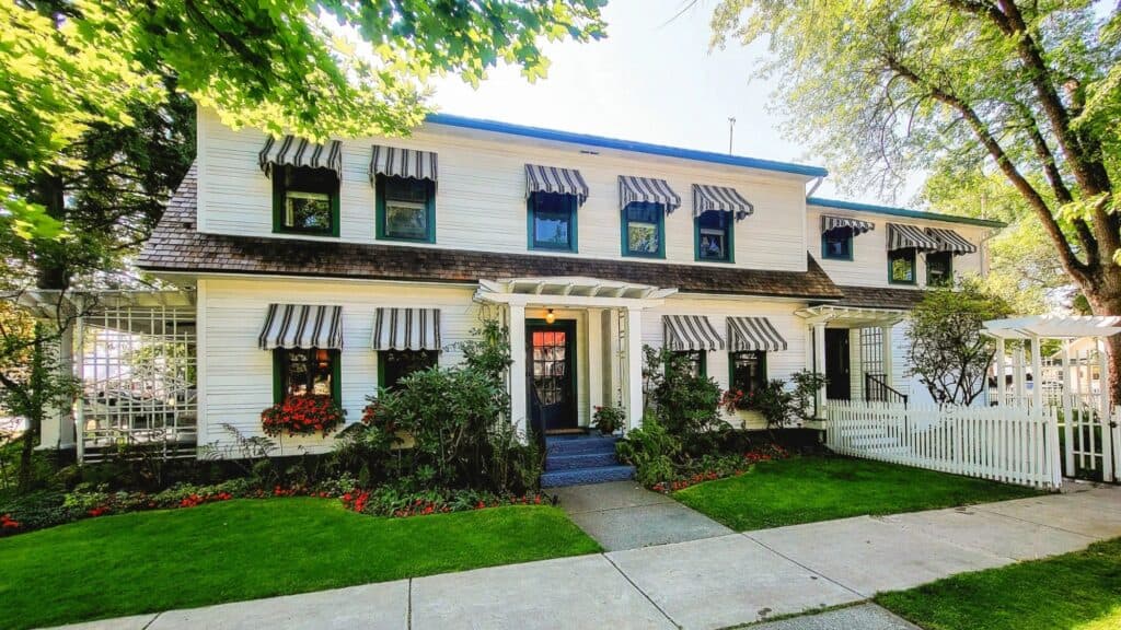 Two-story white house in the Whitefish range, featuring black and white striped awnings, flower boxes, and a front yard with green grass and trees.