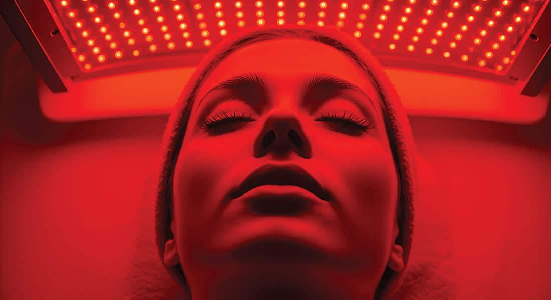 A person lies with eyes closed under a red LED light therapy panel, wearing a headband and appearing relaxed—a scene emblematic of Seattle health and fitness trends as residents embrace innovative wellness treatments for vitality and rejuvenation.