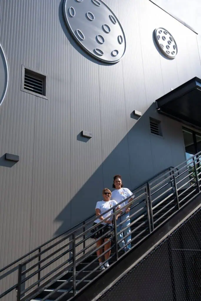 Two people stand on an outdoor staircase next to a gray building with large circular designs on the wall.