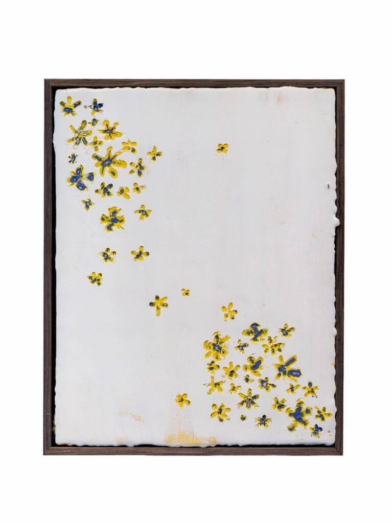 Rectangular artwork with a white background featuring scattered yellow and blue small flower shapes, mostly concentrated in the upper left and lower right corners. Framed in a thin dark frame.