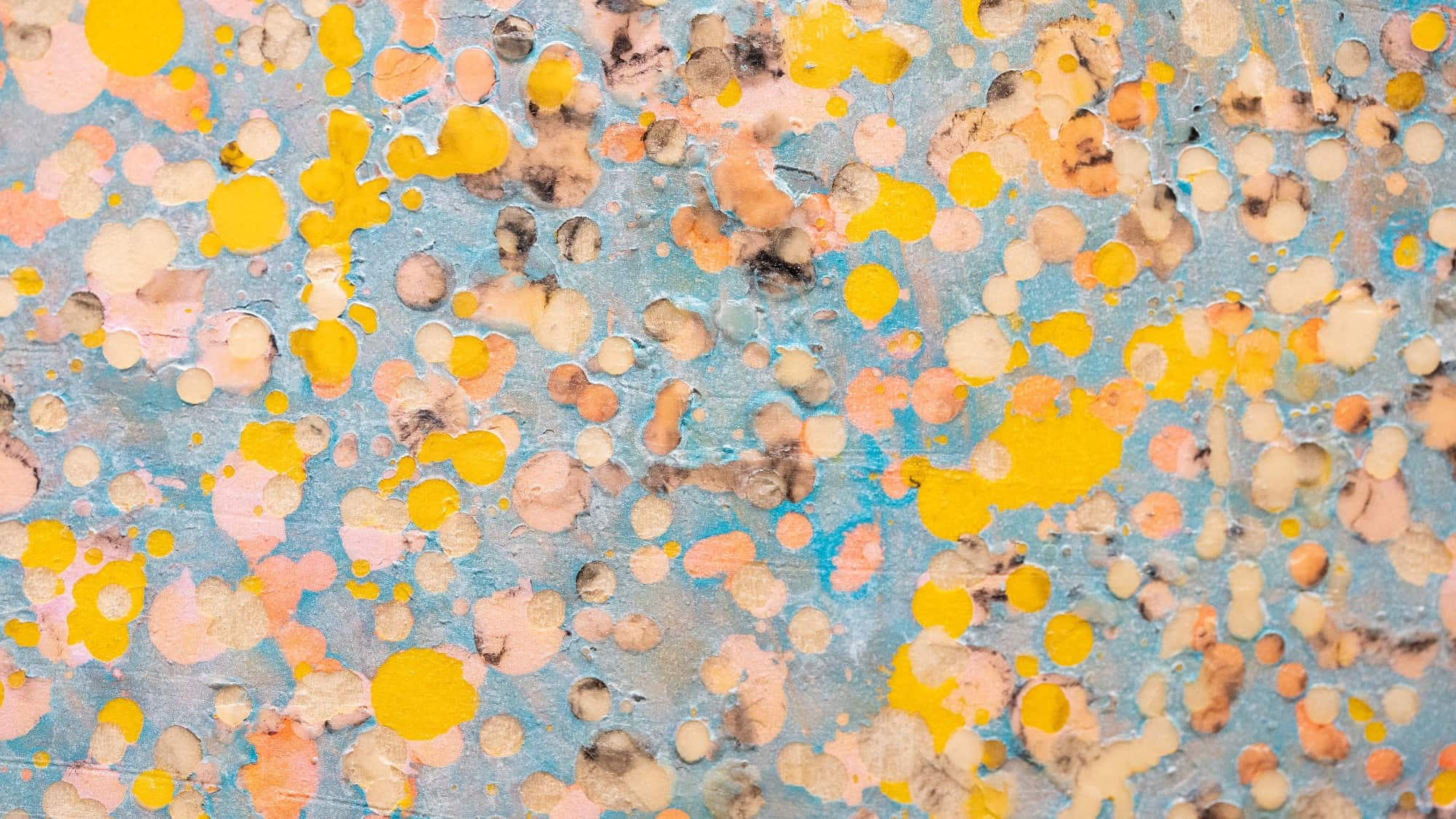 Abstract painting with yellow, peach, and brown splatters and dots on a light blue background, creating a textured and layered appearance.