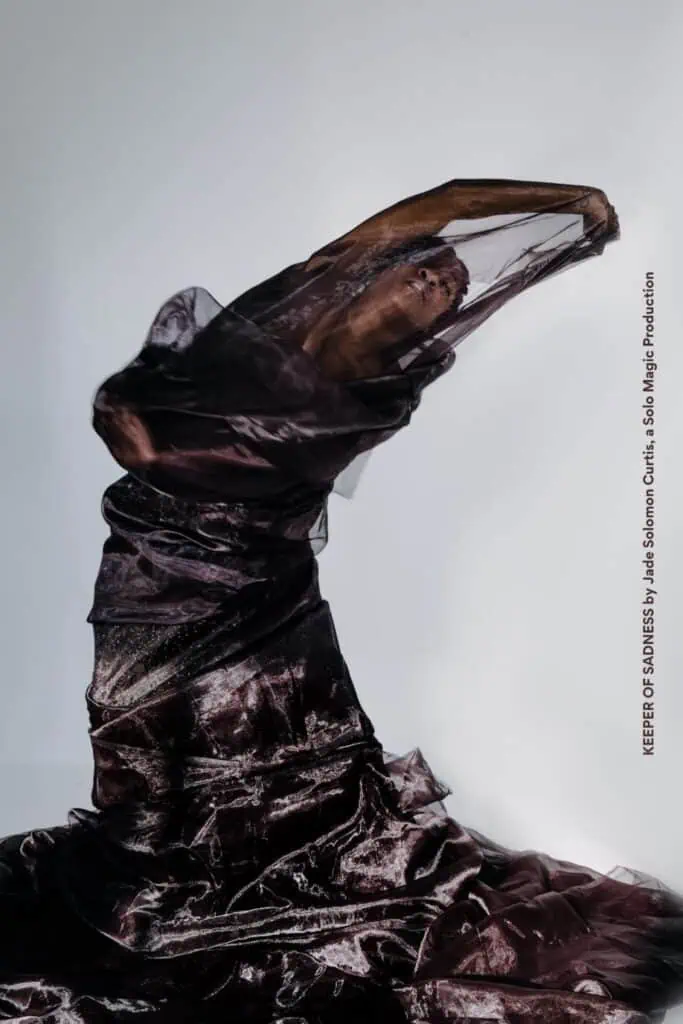 A person poses wrapped in flowing, semi-sheer dark fabric against a plain white background. Text on the right side reads: "KEEPER OF SOUNDS by Leslie Salomon Cristó Solo Life Production.