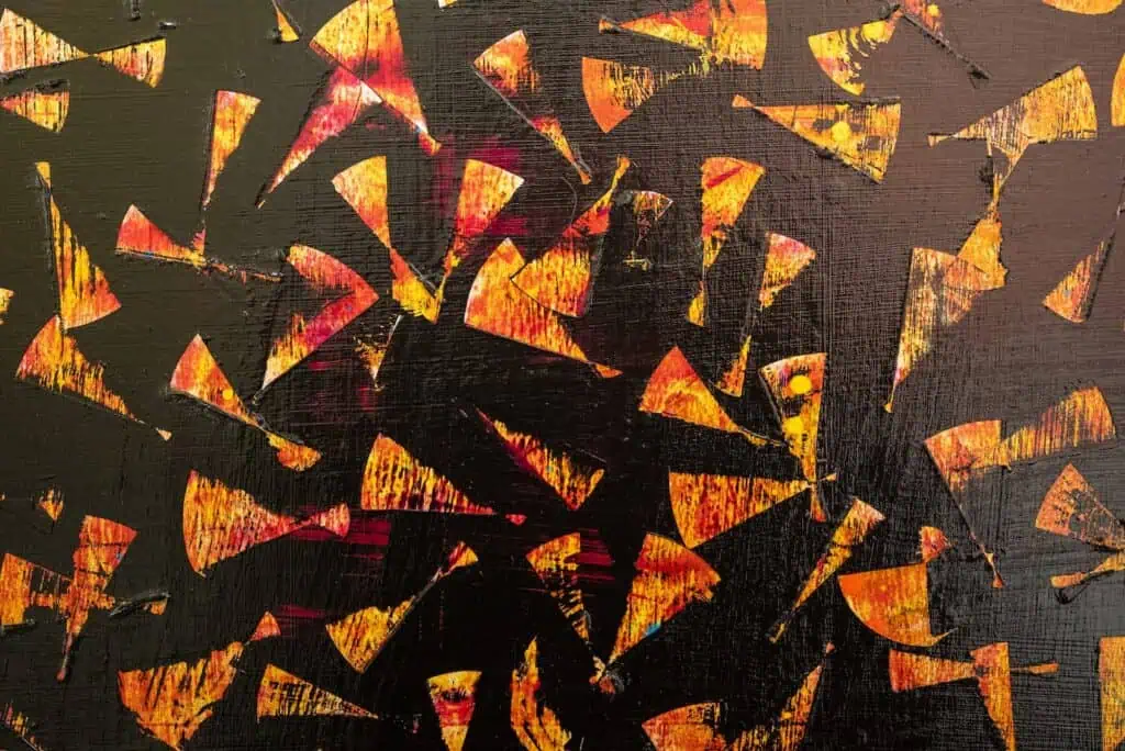Abstract painting with scattered orange and yellow triangular shapes on a black background, creating a dynamic, textured pattern.