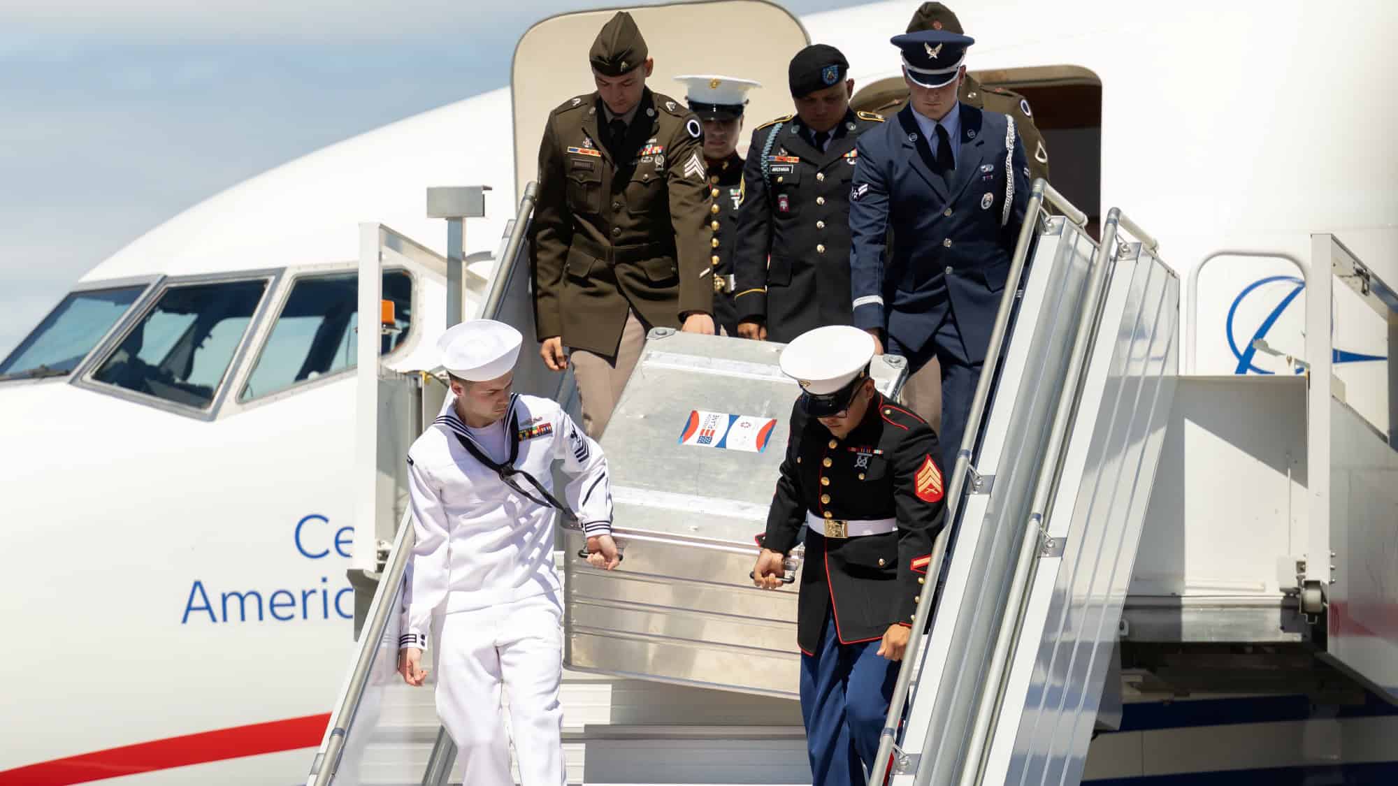U.S. military personnel carry a flag-draped transfer case down airplane stairs during a poignant repatriation ceremony, honoring the values enshrined in the US Constitution and the Bill of Rights as the nation approaches its United States 250th anniversary.