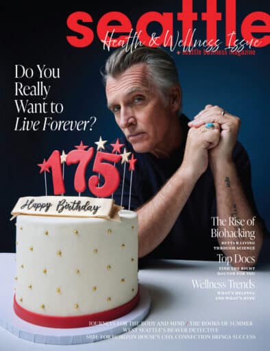 A man sits at a table with a white birthday cake featuring red candles forming "175" and a "Happy Birthday" sign, on the cover of Seattle magazine's Health & Wellness Issue.