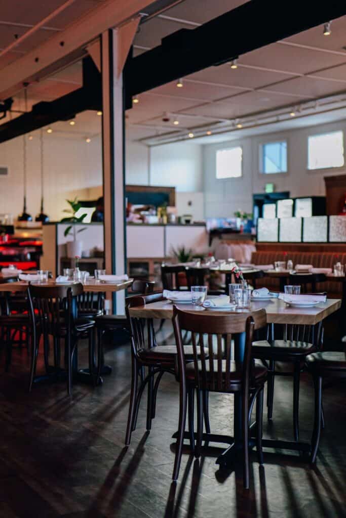 A modern restaurant dining area with empty tables and chairs, set with glassware and napkins, in natural and artificial lighting—a welcoming space curated by Chef Nick Green at Island Reset on Vashon.