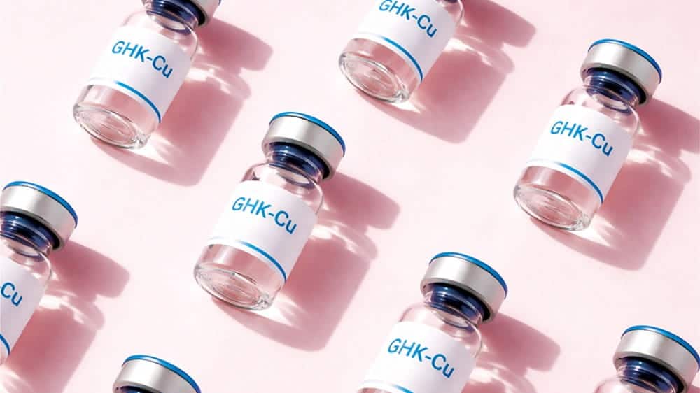 Multiple clear glass vials labeled "GHK-Cu" with blue caps are arranged in a diagonal pattern on a pink surface, reflecting the latest Seattle health and fitness trends focused on innovative wellness solutions.