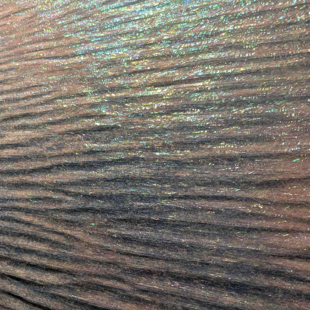 Close-up of a textured surface with horizontal ridges, reflecting iridescent light in shades of blue, green, and hints of pink.