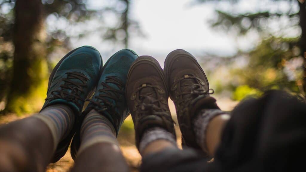 Two people wearing hiking shoes and patterned socks sit side by side outdoors, with their feet extended in front of them and trees visible in the blurred background—capturing a peaceful moment while exploring Washington trails.
