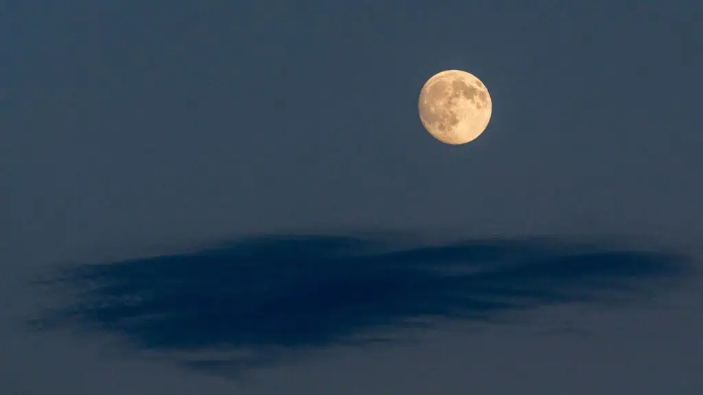 The full moon shines brightly in a clear evening sky above a dark, wispy cloud—perfect for a peaceful weekend in Carlsbad, California.