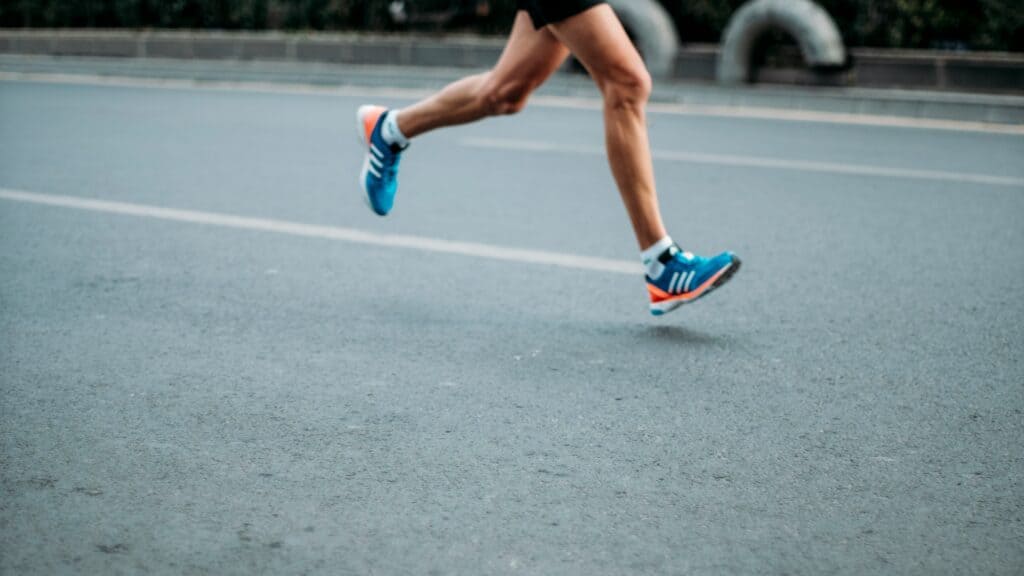A person wearing blue running shoes and black shorts runs on an empty paved road, with only their legs visible in the frame—a scene reflecting the latest Seattle health and fitness trends.