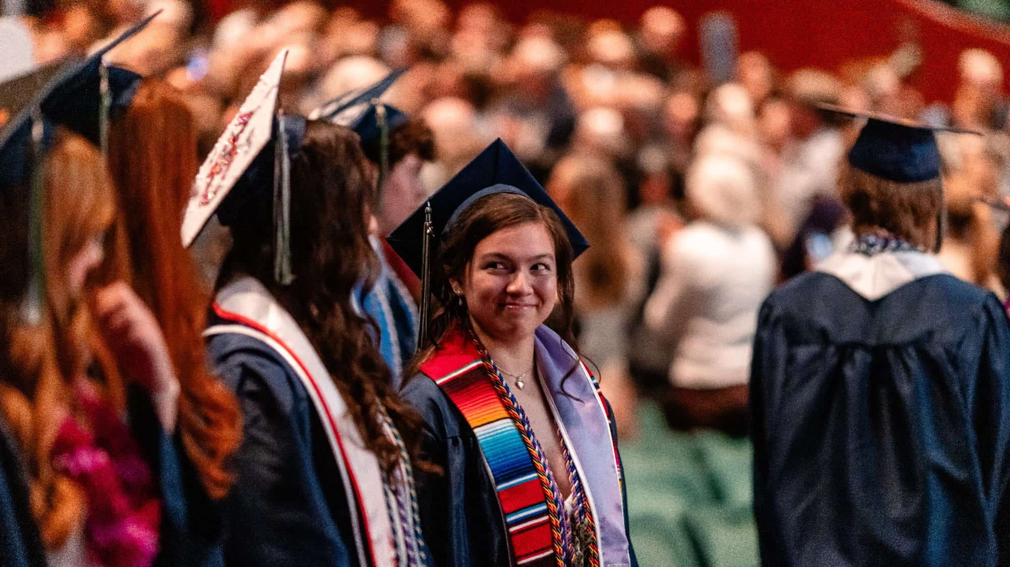 Graduates in caps and gowns stand in a row during a ceremony, with one person in the center wearing a colorful stole and smiling at another graduate—a celebration of finding their best-fit university, perhaps thanks to UPrep’s expert college planning tips.