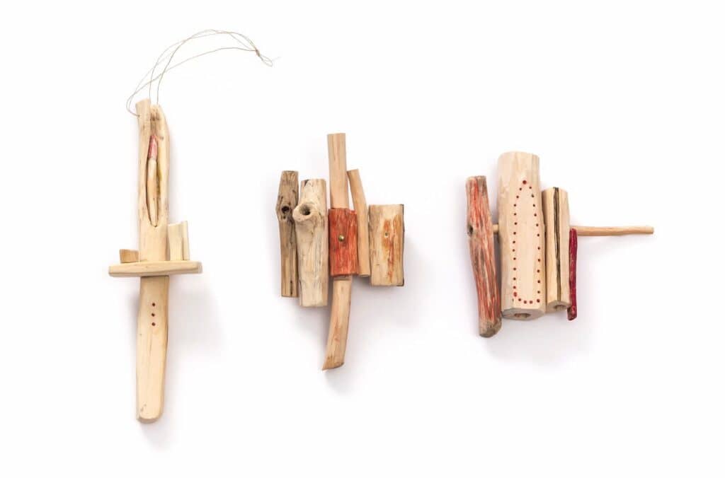 Three handmade wooden objects with drilled holes and reddish markings are arranged side by side on a white background.