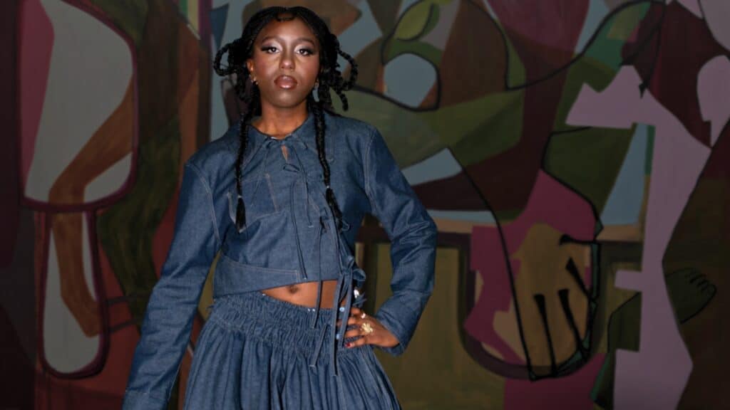 Woman in a blue denim outfit poses confidently in front of a colorful abstract mural.