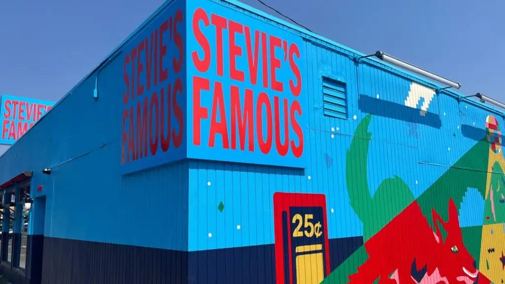 A bright blue building with large red text reading “STEVIE’S FAMOUS” and colorful murals stands out in North Seattle; a sign shows “25¢”.