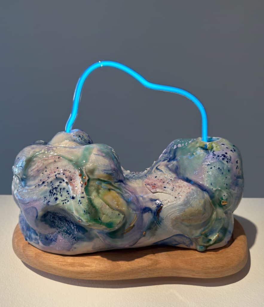 Abstract ceramic sculpture with pastel swirls on a wooden base, featuring a blue neon tube looping across the top.