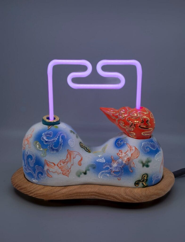 A decorative lamp with a painted ceramic base featuring fish and waves, topped with a red ornament and a glowing purple neon tube.