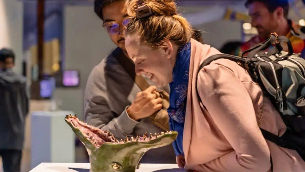 A woman leans in to look closely at a model of a creature’s open mouth while a man stands beside her in an indoor exhibit space.