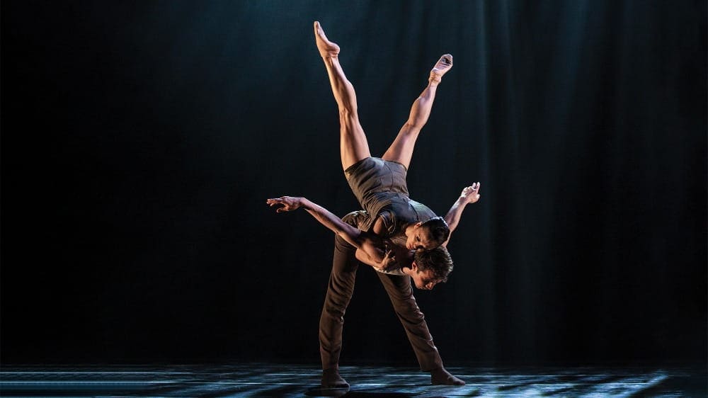 Two ballet dancers perform a lift on stage with dramatic lighting at Seattle’s 5th Avenue Theatre, the female dancer balanced upside down on the male dancer’s back.