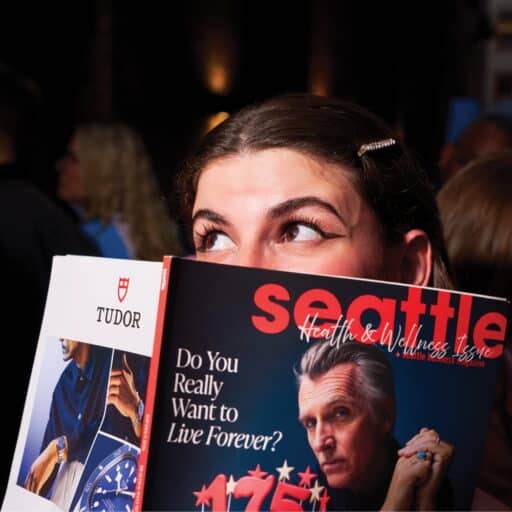 A woman with styled hair holds up a Seattle magazine, partially covering her face, with the headline “Do You Really Want to Live Forever?” visible on the cover—a striking image captured at BP Place.