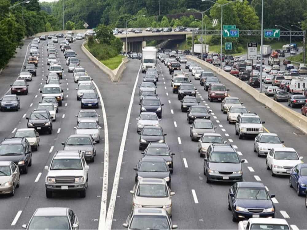 Dense traffic on a multi-lane highway with vehicles moving in both directions, divided by a barrier, and an overpass with more cars in the background—much like the bustling energy of a food court where everyone’s after their favorite burger, or the flowing harmony of a marriage where two paths come together yet remain distinct.
