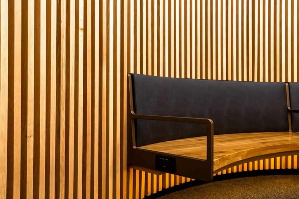 A curved wooden bench with a dark upholstered backrest against a slatted wood wall in a Sea-Tac dining area.