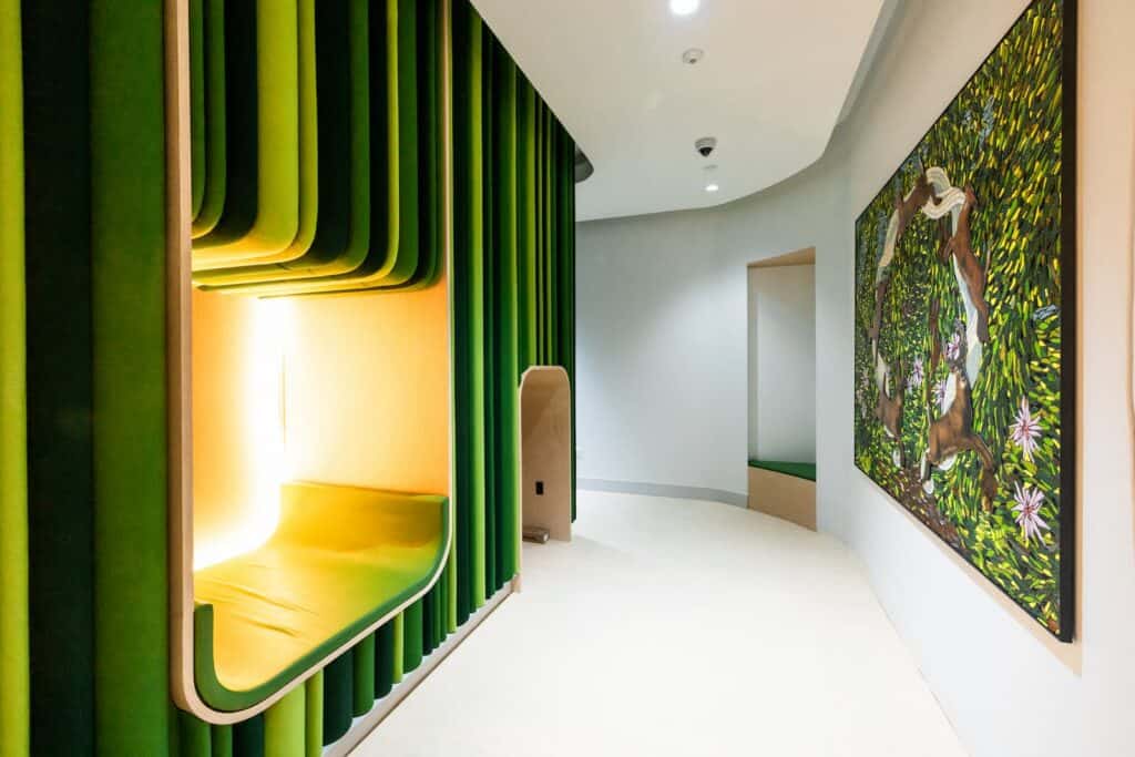 A modern hallway with a recessed green velvet seating nook, a smaller empty alcove, and a large abstract painting of deer on the wall.