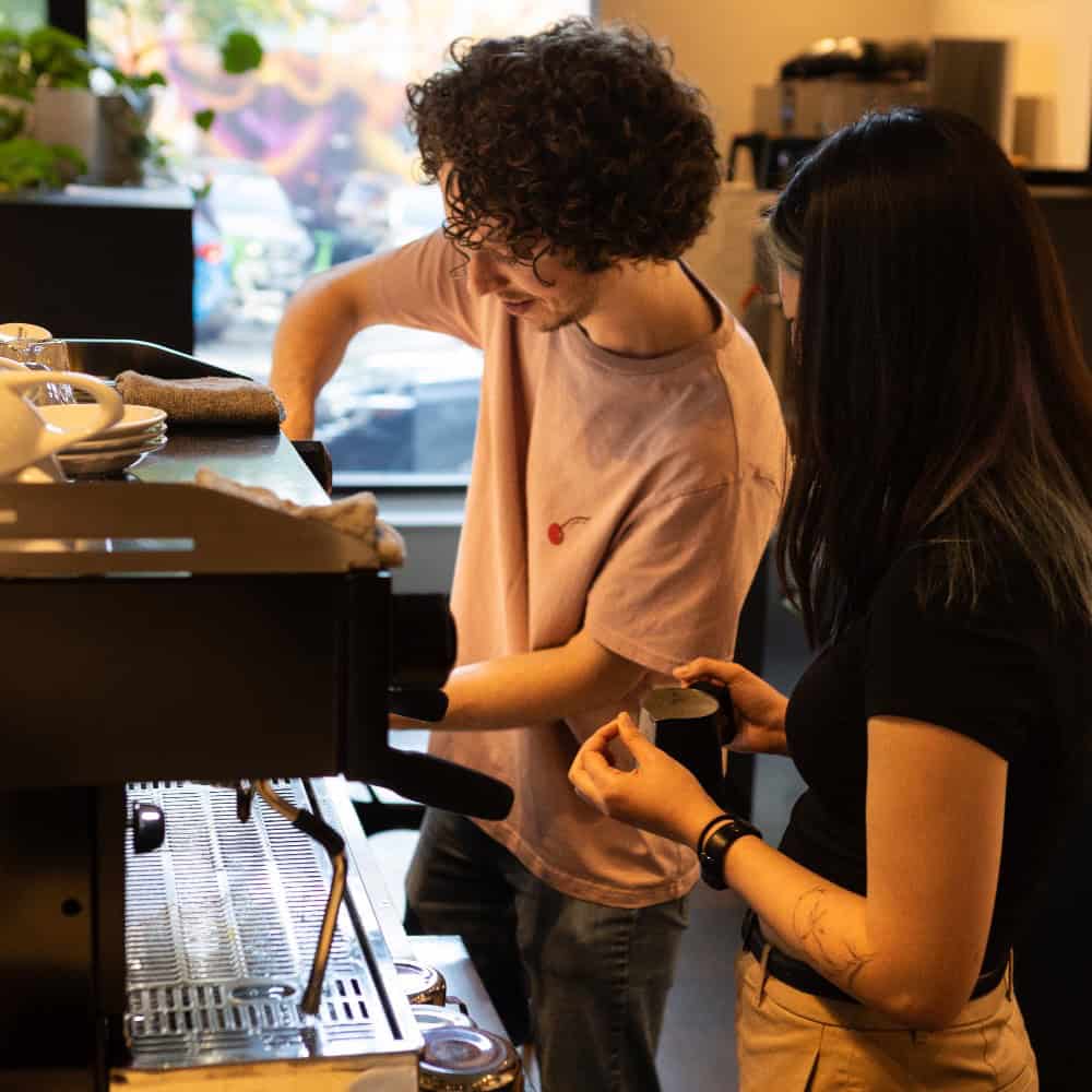 A barista training a person on how to use an espresso machine.