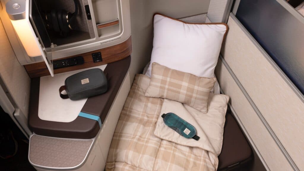 A luxury lifestyle business class seat set up as a bed, including a pillow, blanket, sleep mask, and amenity kit.