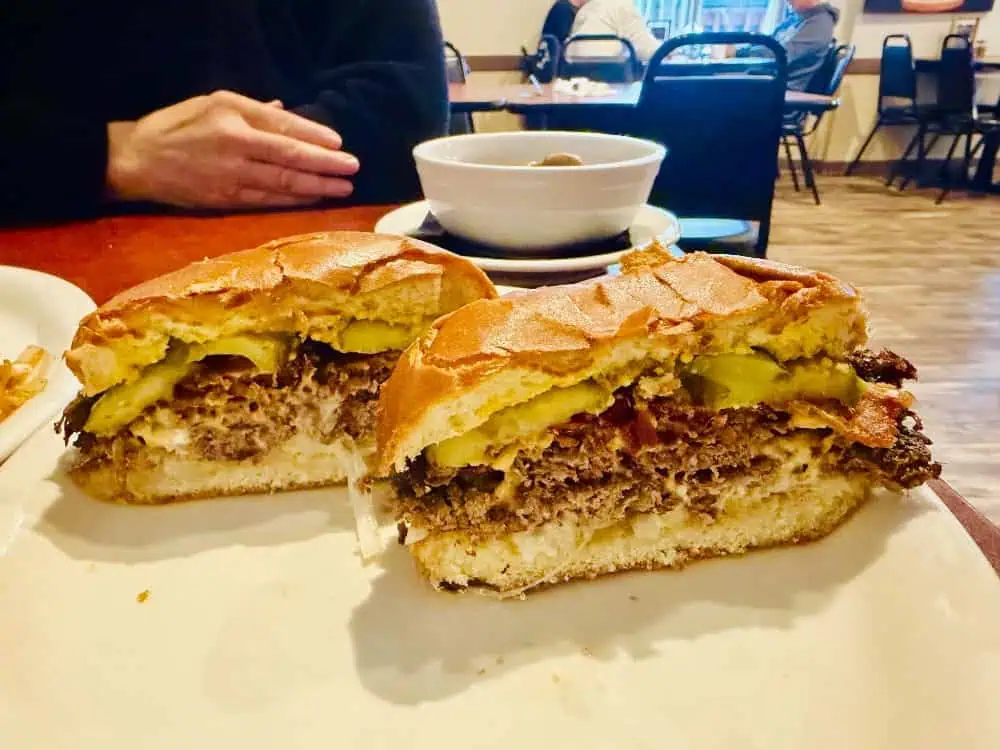 A cheeseburger cut in half on a white plate, served alongside a bowl of soup, making it one of our best burgers.