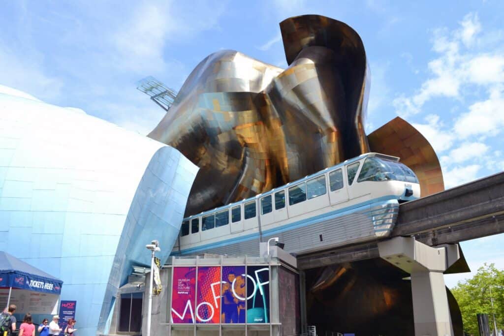 A monorail train passes in front of the Museum of Pop Culture, a building with an abstract, metallic exterior.