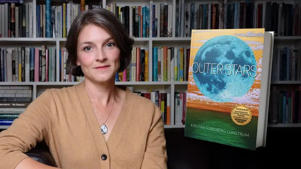 A woman sitting in front of a bookshelf next to a copy of the book “Outer Stars” by Kirsten Sundberg Lunstrum.